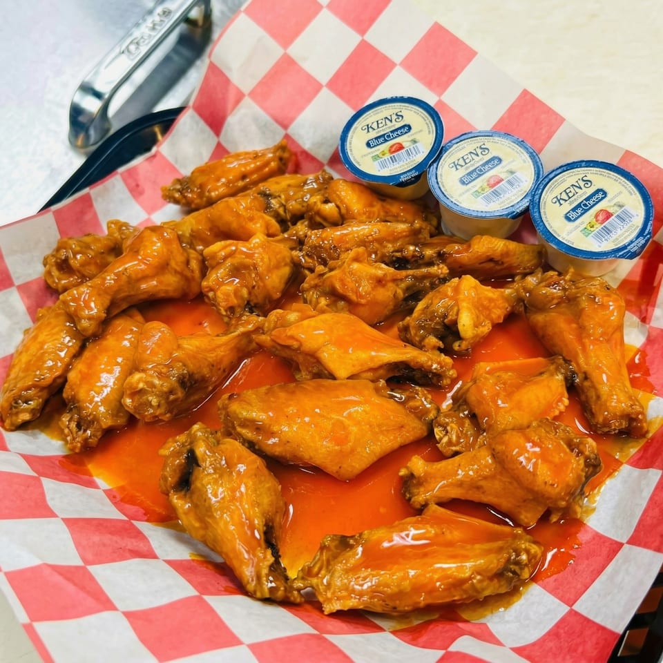 A basket of buffalo chicken wings with three containers of Ken's Blue Cheese dressing.