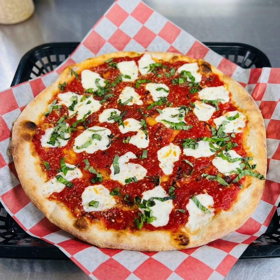 A freshly baked Margherita pizza with bright red sauce, white mozzarella, and green basil on checkered paper.
