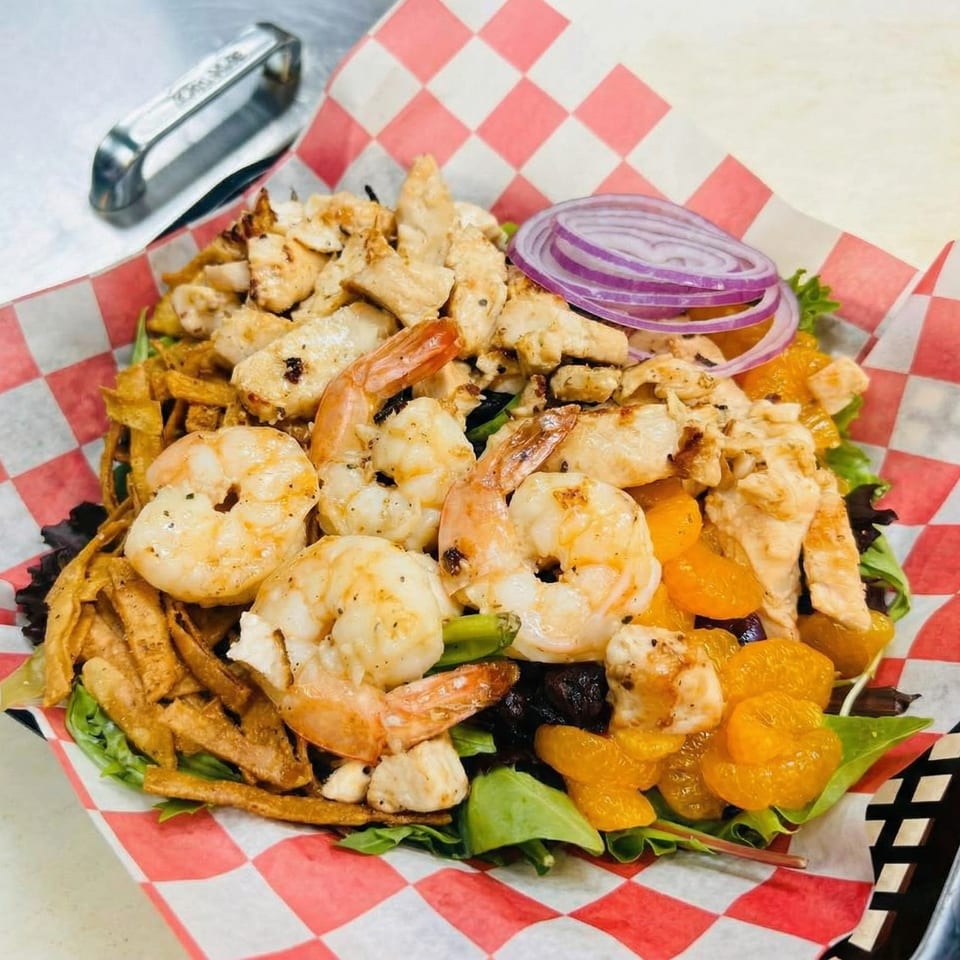 A vibrant salad with grilled chicken, shrimp, mandarin oranges, red onion, and crispy wonton strips.