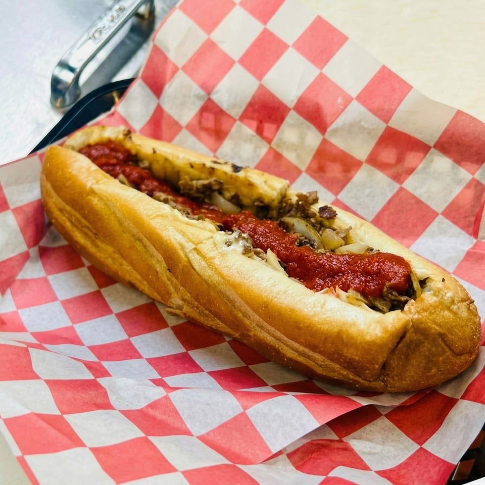 A cheesesteak sandwich with red sauce and onions on a red and white checkered paper.