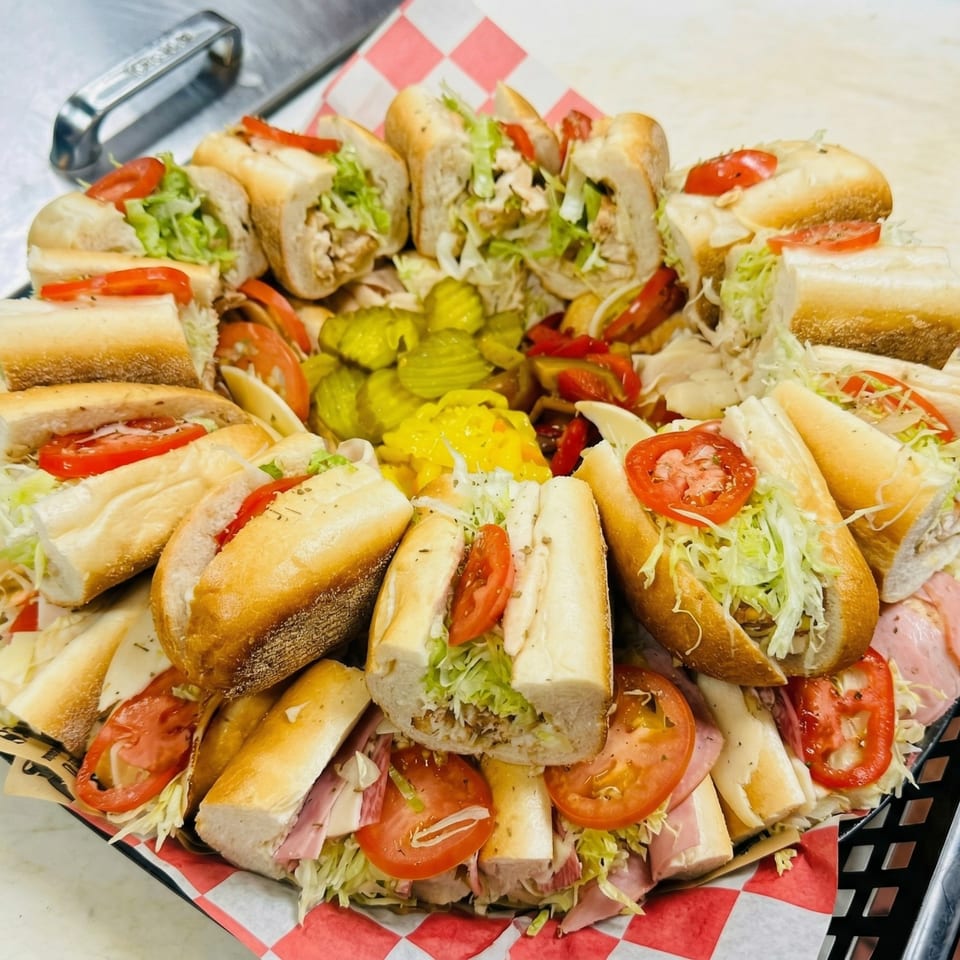 A platter of various submarine sandwiches, cut in half, with pickles and peppers.