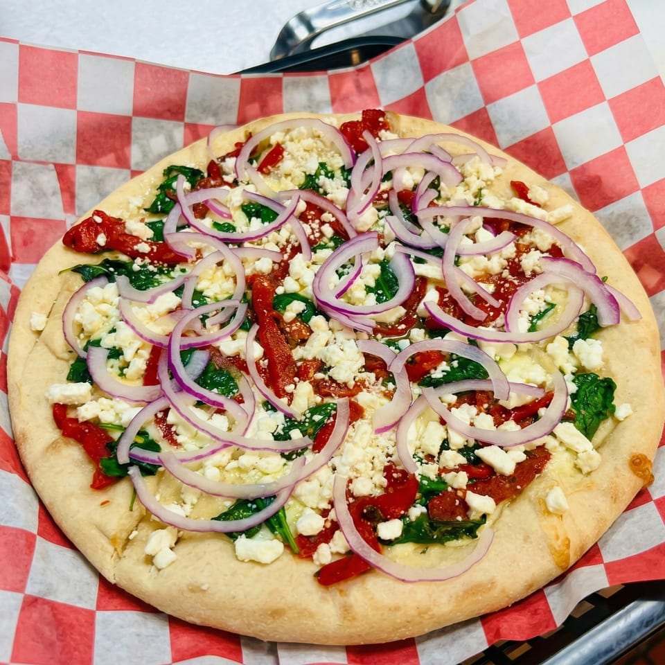 A flatbread pizza with spinach, sun-dried tomatoes, feta cheese, and red onion slices.