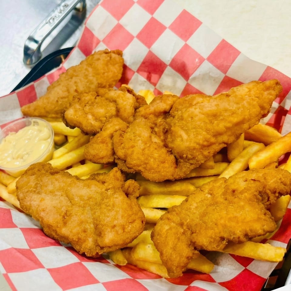 Crispy fried chicken tenders and golden french fries served in a red and white checkered basket with dipping sauce.